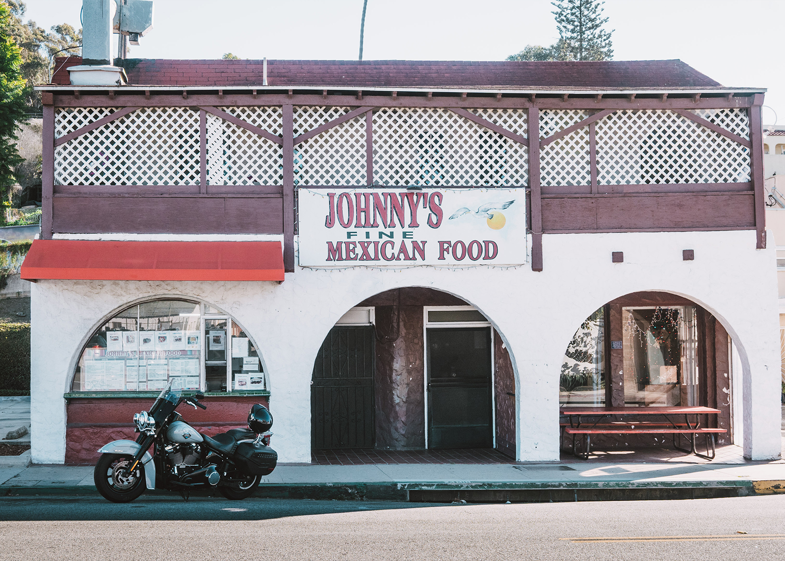 A Harley-Davidson Heritage Classic motorcycle parked outside Johnny’s Fine Mexican Food restaurant with red awning and arches