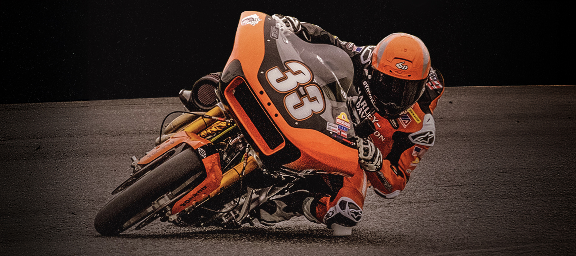 Kyle Wyman drags his knee on the ground while riding his orange HD Bagger around a tight curve. 