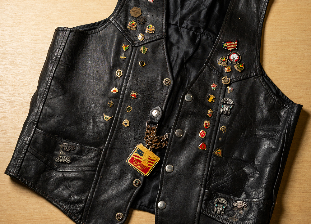 Black leather vest laid flat on a table, covered with colorful pins, badges, and stitched details