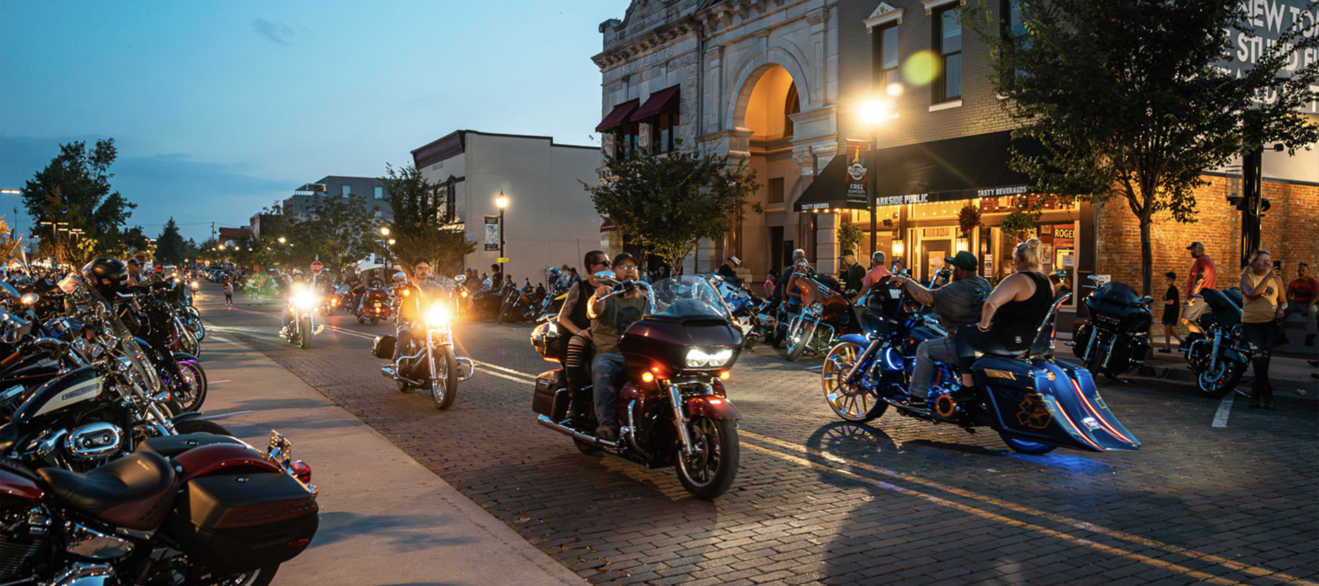 A group of riders rides down a bricked street at dusk