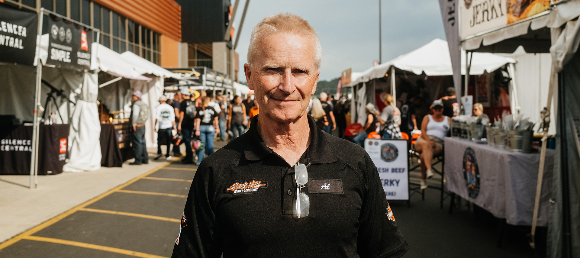 Black Hills Harley-Davidson General Manager Al Rieman stands smiling among vendor tents at a busy motorcycle rally.