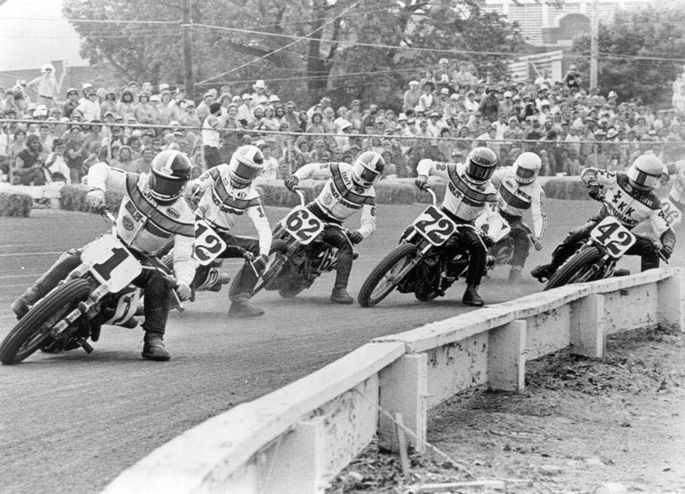 Number 1 rider Jay Springsteen leads a pack of flat track racers battling for position through a corner as spectators look on