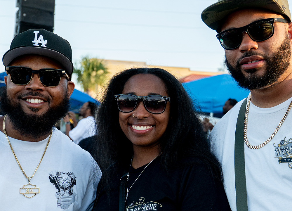 Small group stands together near parked motorcycles at a lively street event under clear daylight