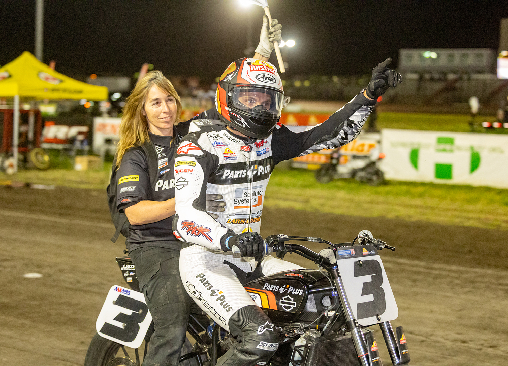 Briar Baumann celebrates atop a race bike in the infield after a flat track podium finish