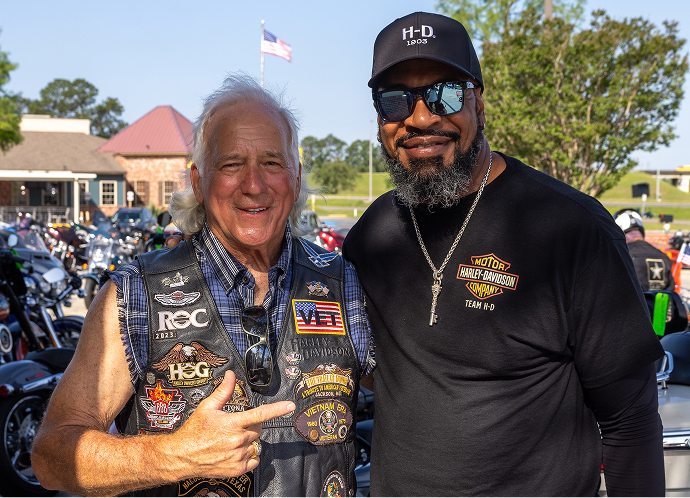 Two riders stand side by side near parked motorcycles, posing for a photo during a rally gathering
