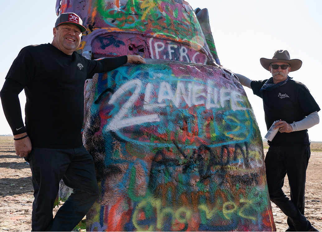 2LaneLife crew standing beside a colorful, graffiti‑covered car installation in a desert setting