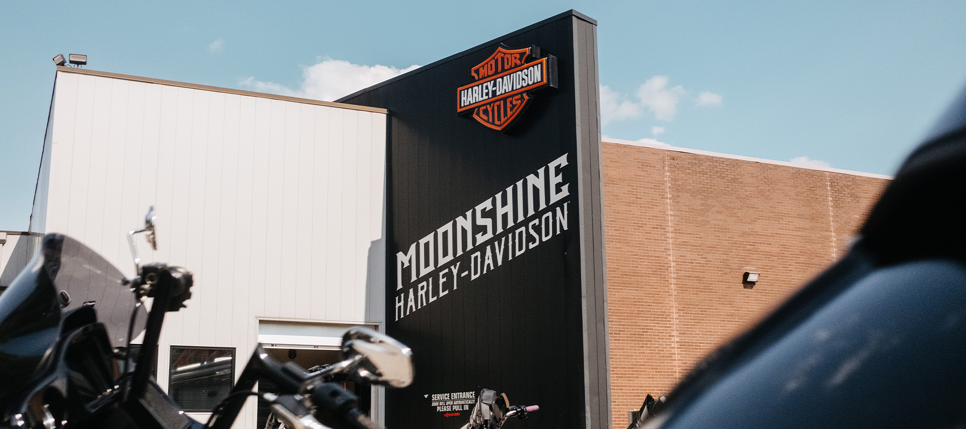 Looking up at the exterior signage of Moonshine Harley-Davidson dealership with motorcycles in the foreground.