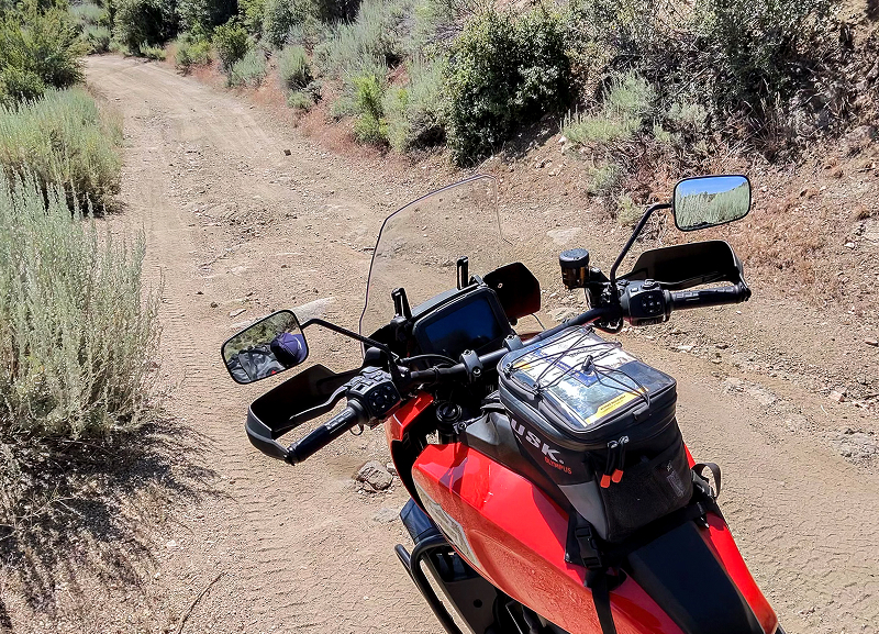 Handlebar view of Red H-D Pan America motorcycle on narrow dirt trail with phone mount and tank bag visible