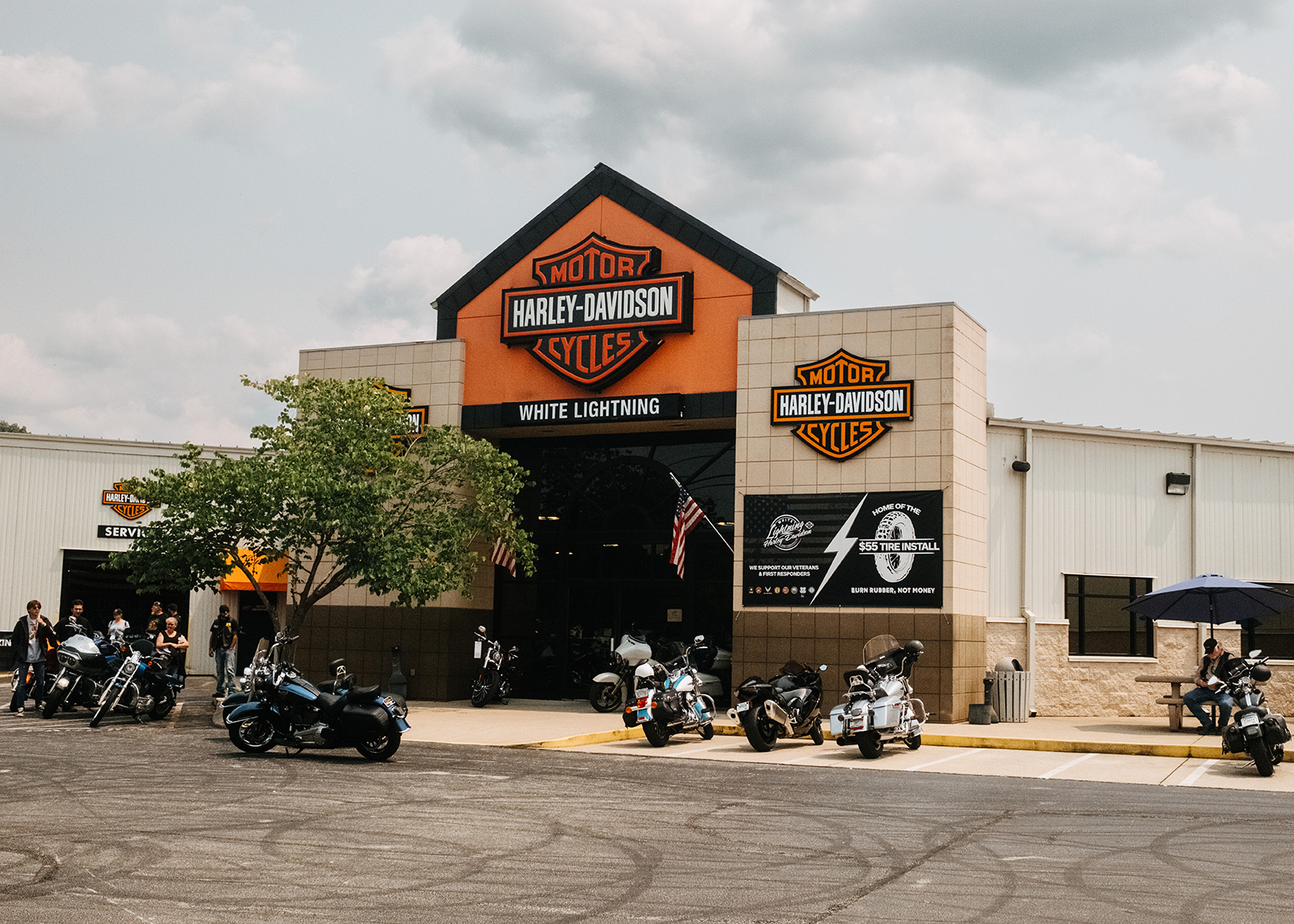 Parked motorcycles and riders outside of the entrance to White Lightning Harley-Davidson.
