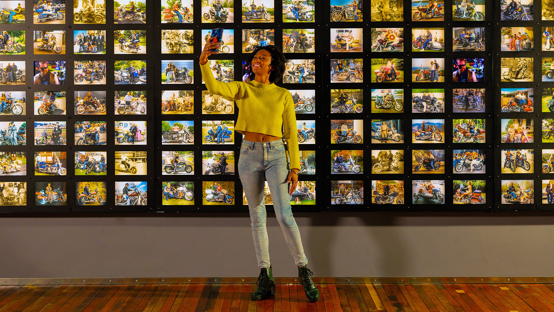 Person taking selfie in front of wall filled with motorcycle photos