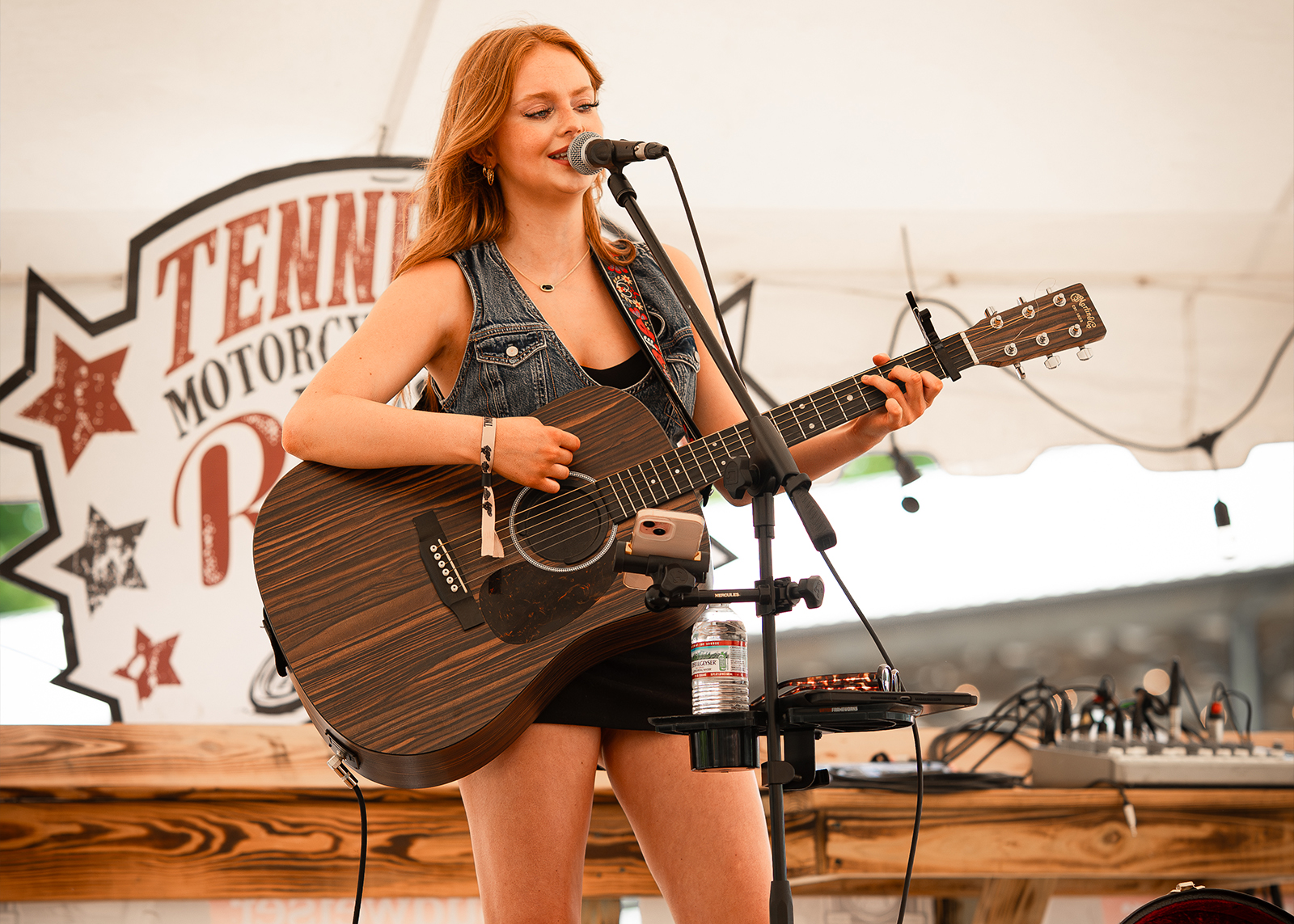 A woman on stage plays her guitar and sings into a microphone.