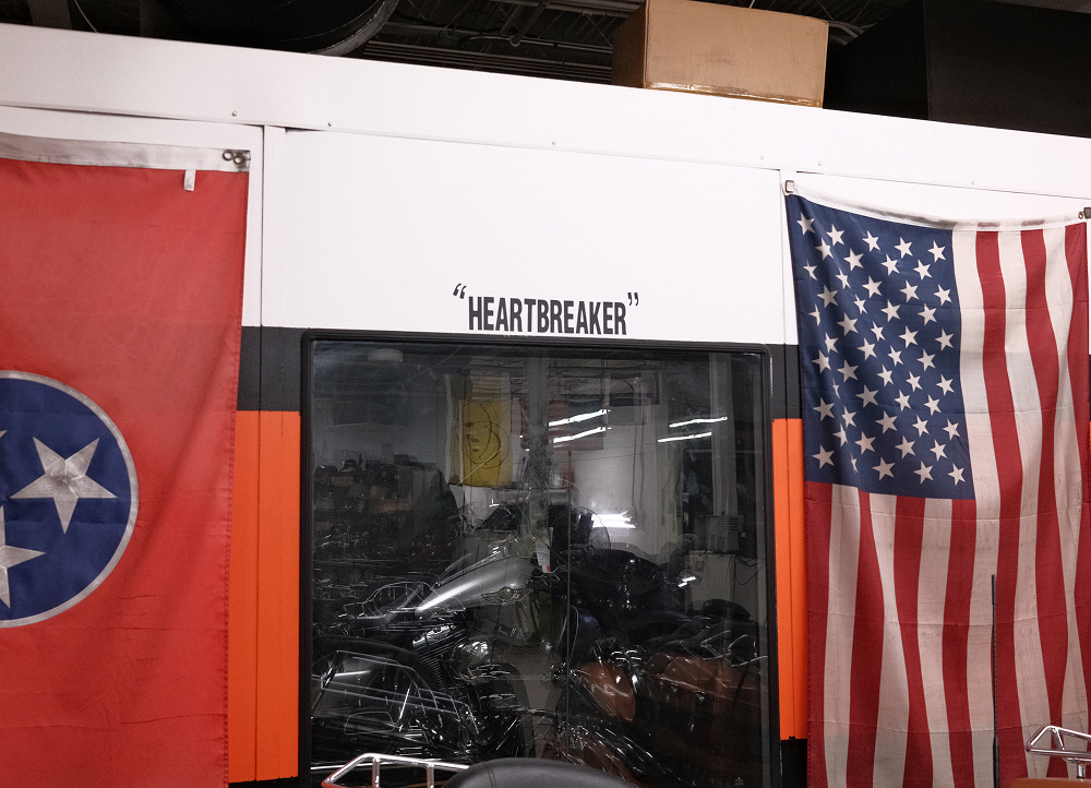 View through a service window into a motorcycle workshop, framed by American and Tennessee flags