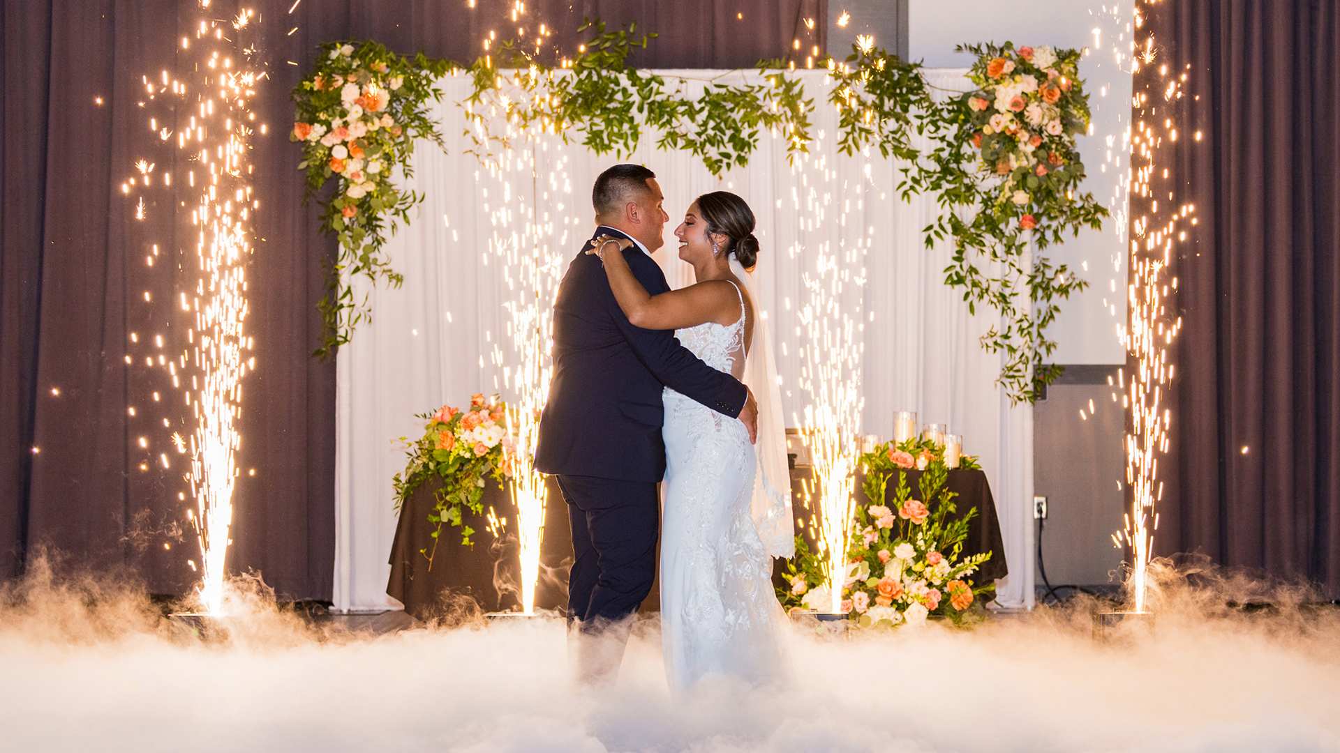 Wedding couple dancing beneath spark effects and floral arch