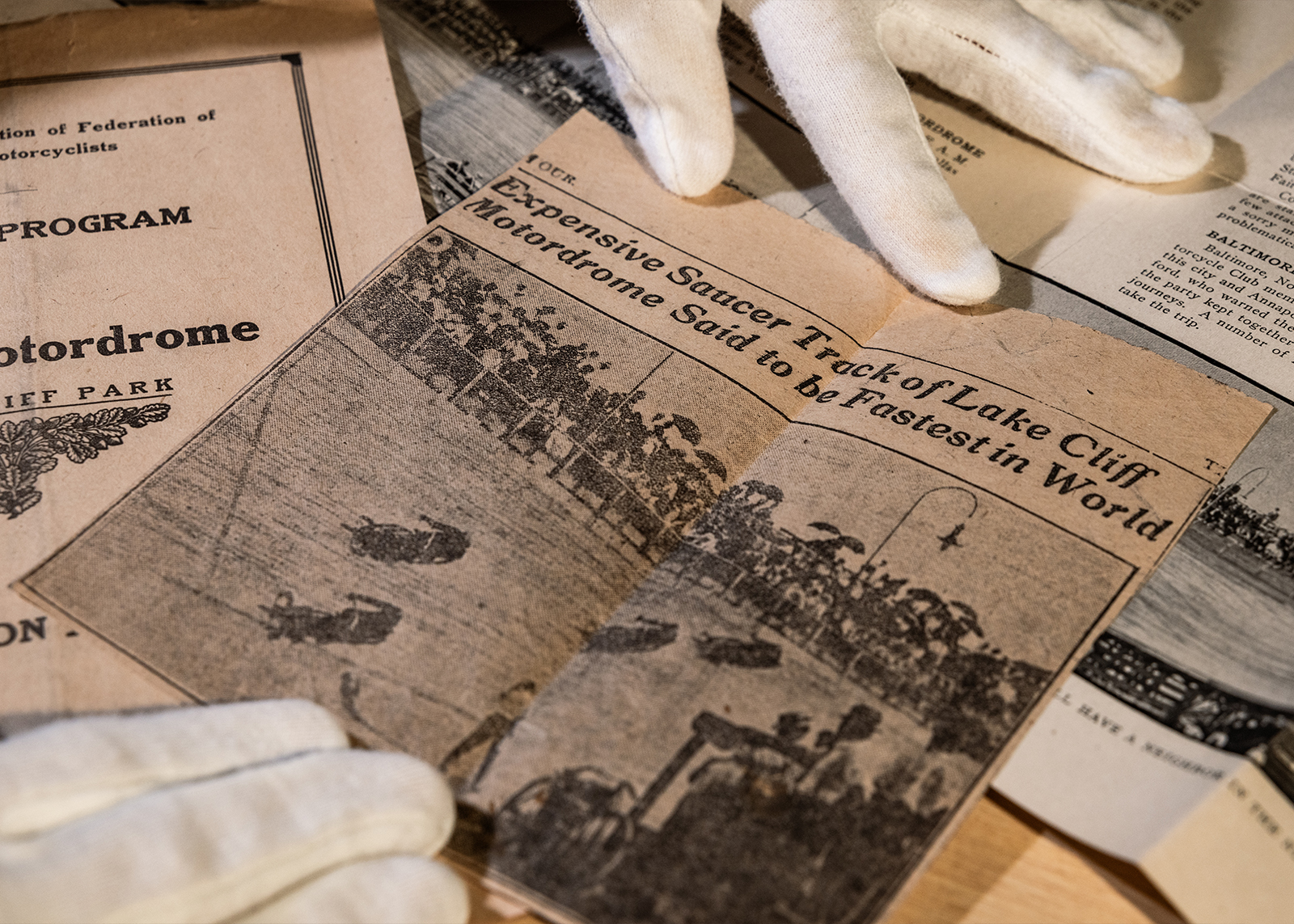 Vintage newspaper clipping with photo of board track race and headline “Expensive Saucer Track of Lake Cliff Motordome Said to be Fastest in the World”