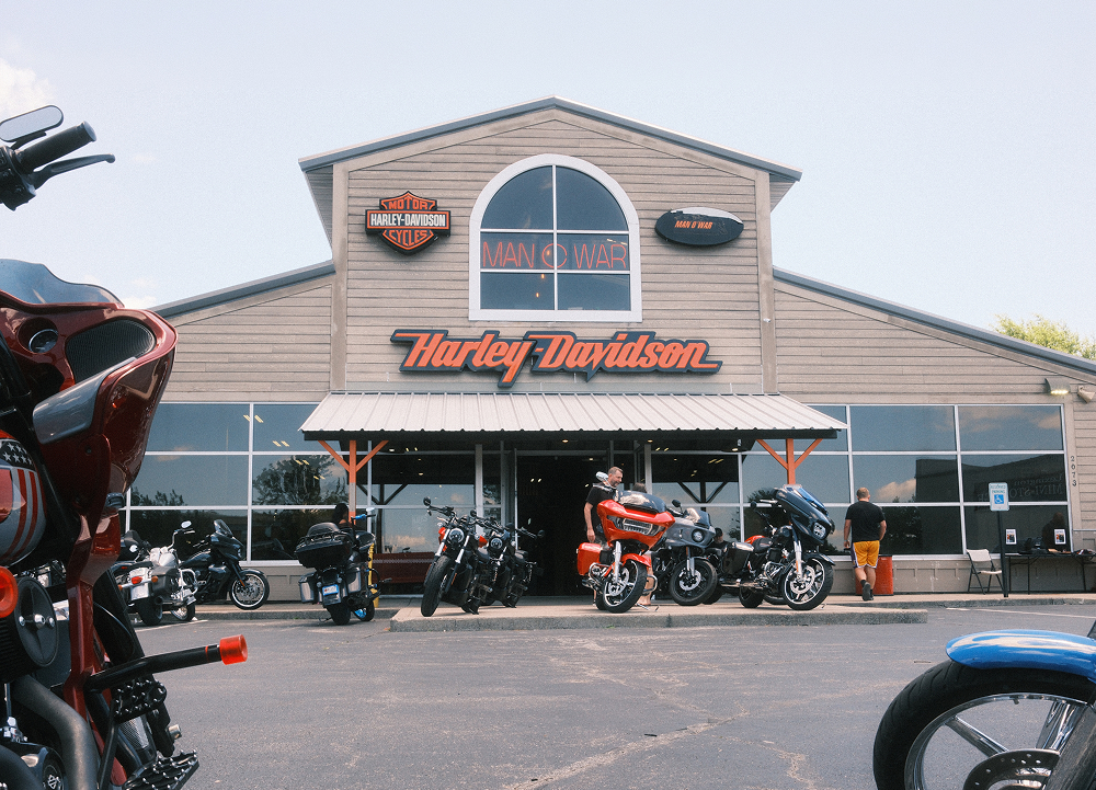 Man O’ War Harley-Davidson dealership storefront with touring motorcycles parked outside and riders gathering near the entrance