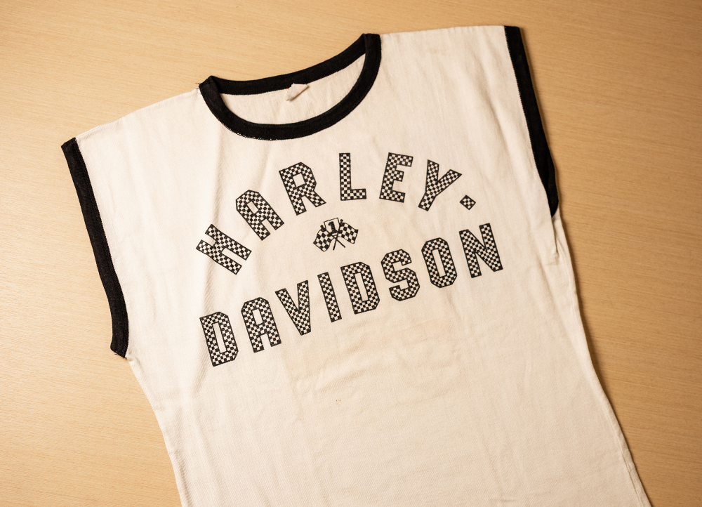 Sleeveless white Harley‑Davidson shirt laid flat on a table, showing bold black lettering and ribbed trim