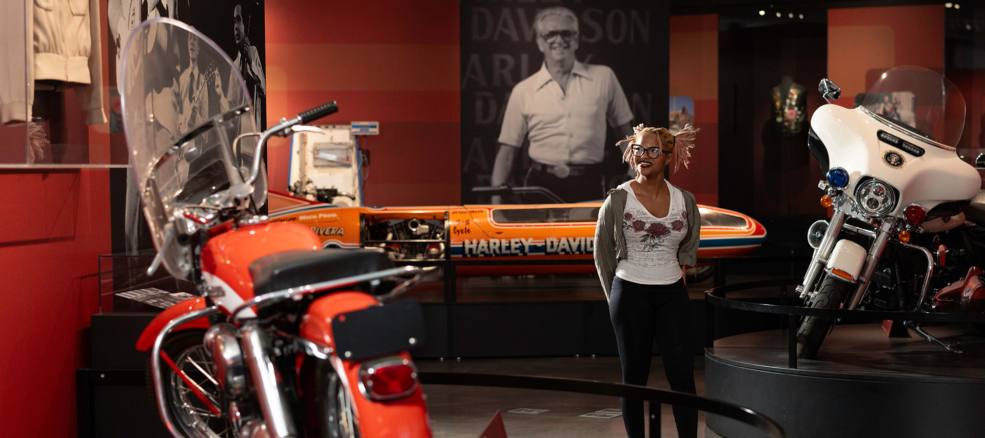 Visitor standing near vintage motorcycles and large archival display in museum