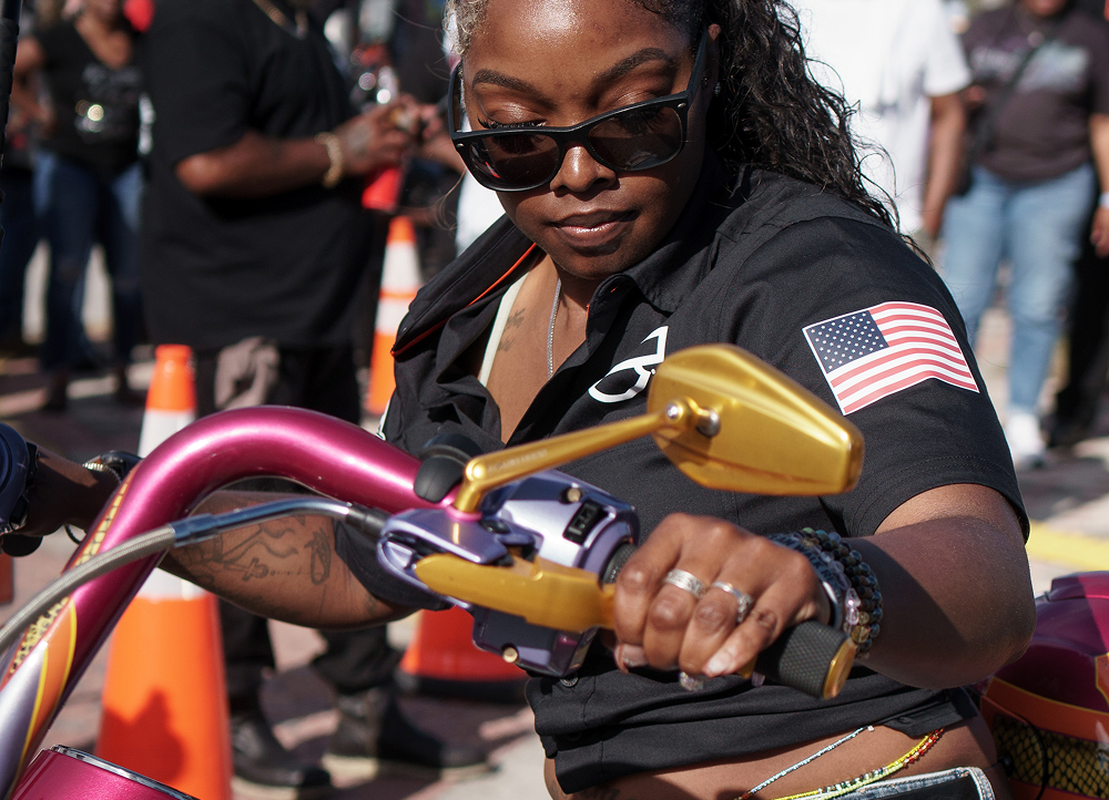 A rider maneuvers a motorcycle with colorful handlebars, with street barricades and spectators in the background