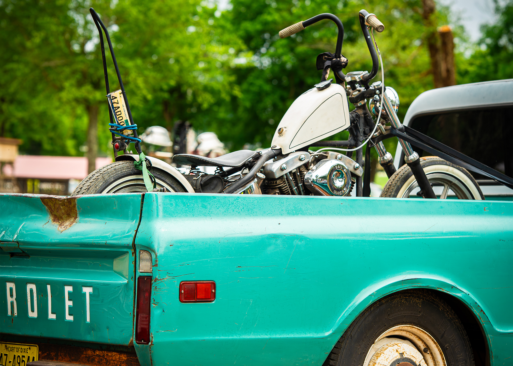 A turquoise pickup truck with a white Harley parked in the bed.