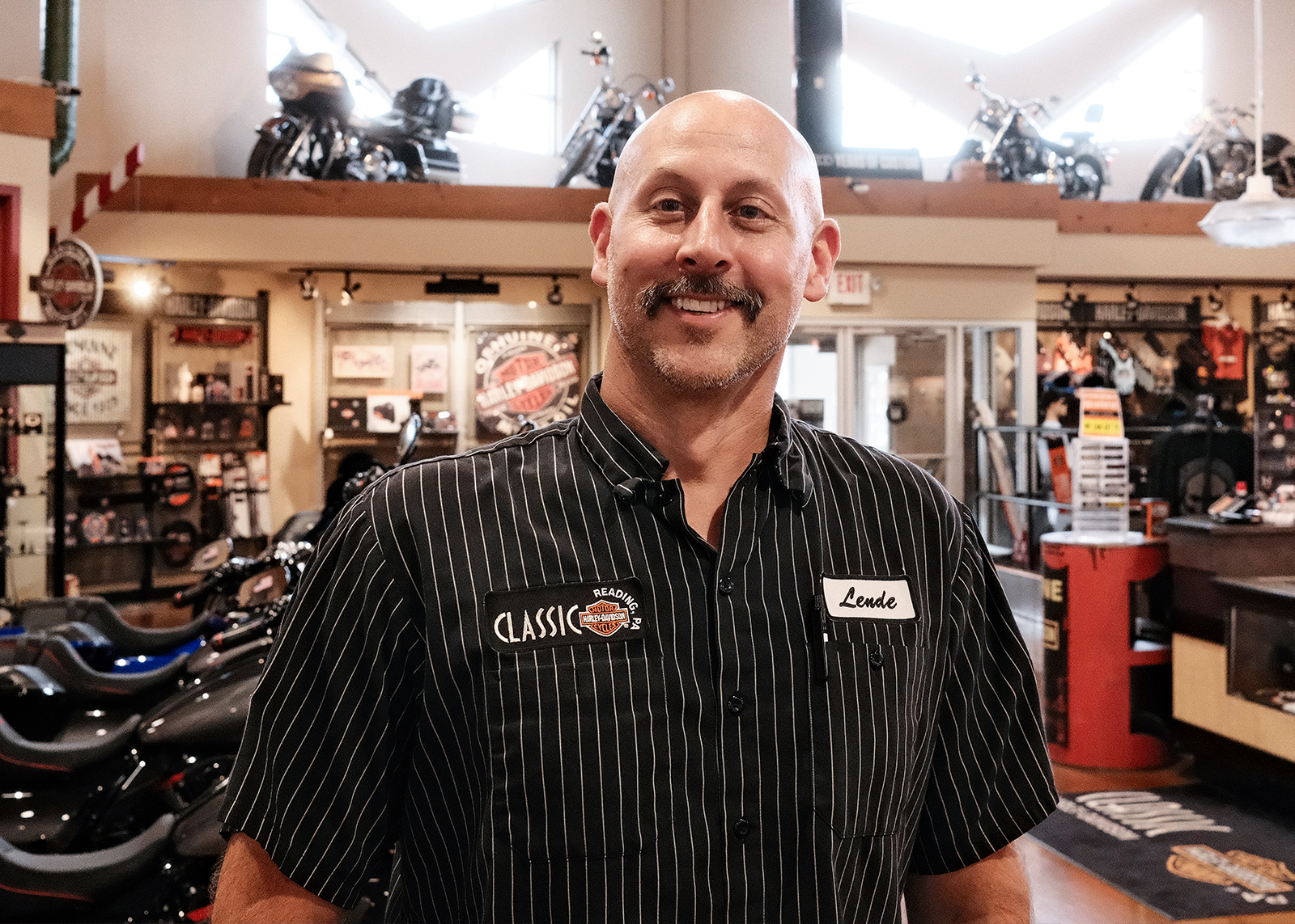 A staff member wearing a black pinstriped shirt smiles at the camera.