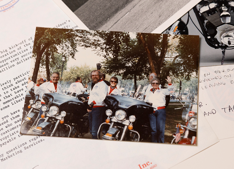 Vintage printed photo of a group posed with motorcycles, placed atop handwritten notes and documents