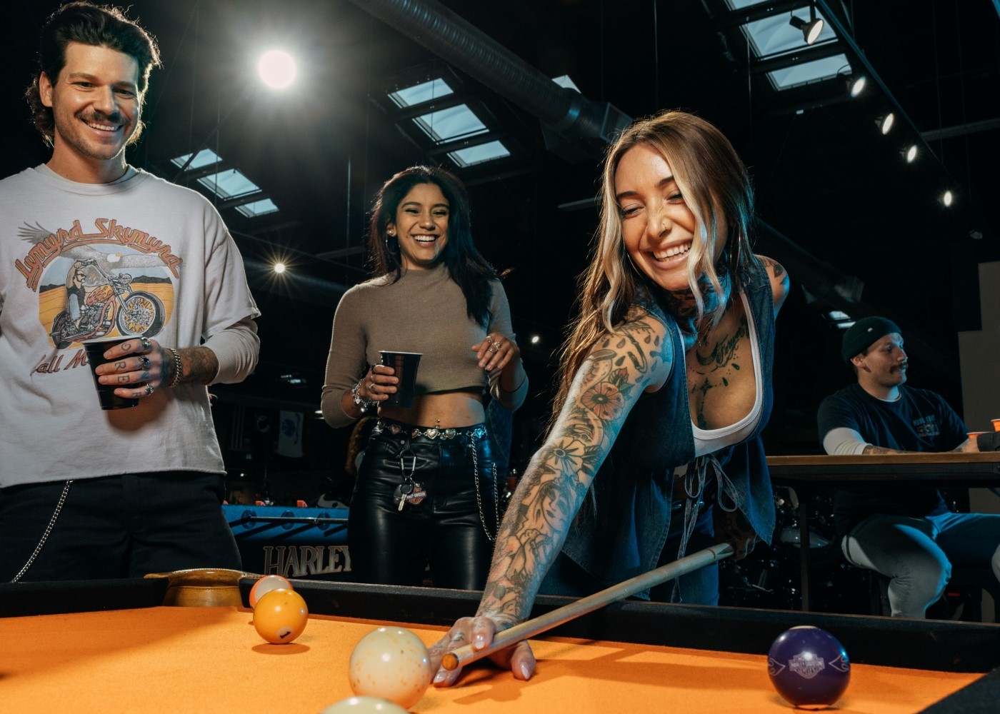Gruppo di amici che ride e si diverte mentre una donna effettua un tiro a biliardo durante una delle Harley Nights.