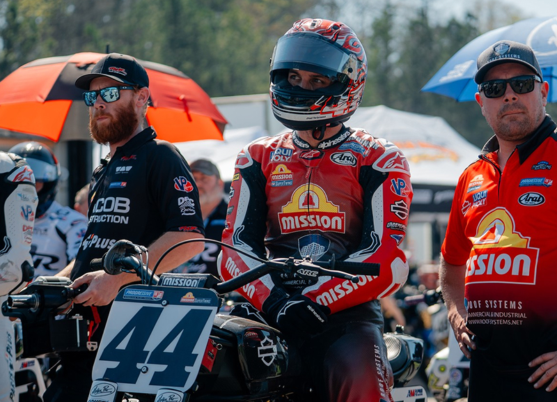 Brandon Robinson sits aboard motorcycle #44 in the paddock, surrounded by crew and race equipment