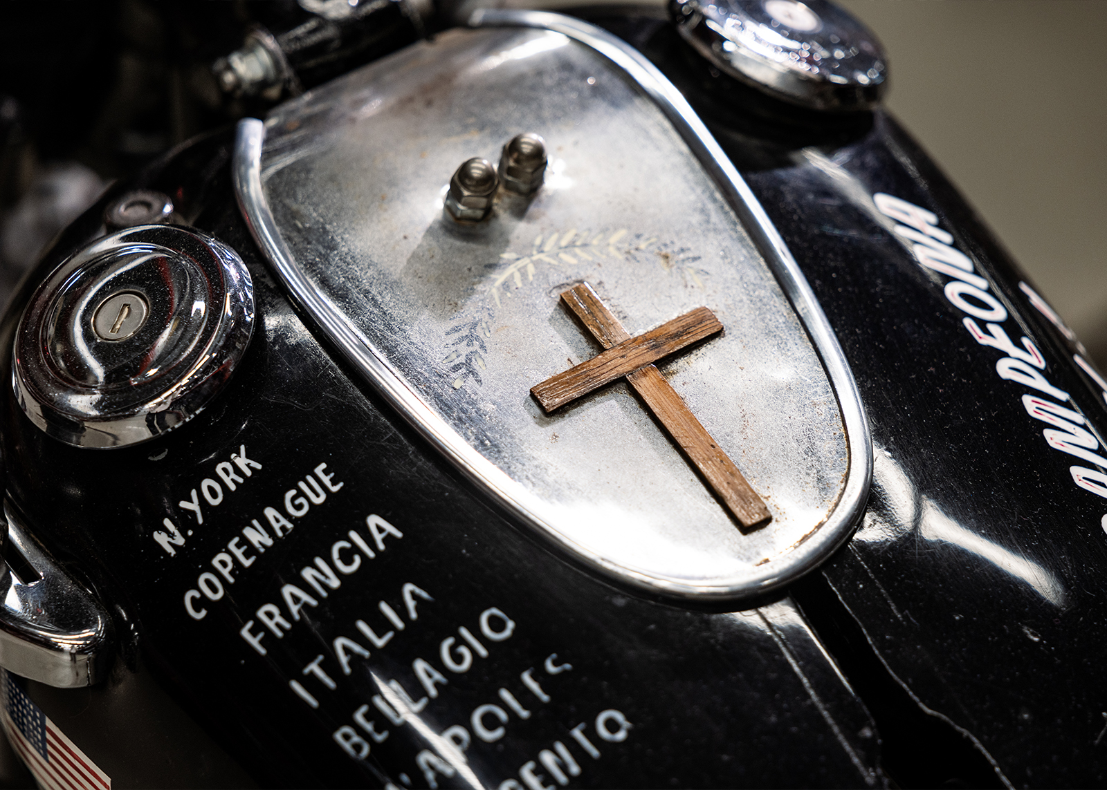A close up of the tank of Alfonso Sotomayor’s 1957 Harley-Davidson FL showing hand painted text and a wooden cross mounted on a silver panel.