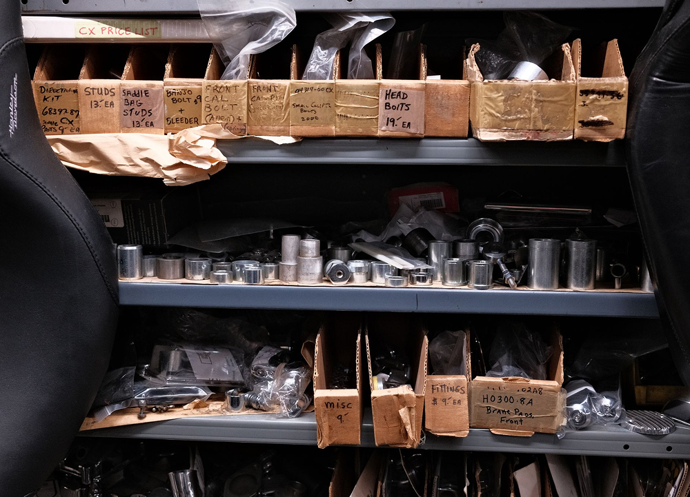 Organized shelves of small machined parts and labeled boxes in workshop storage area with bins and hardware tools