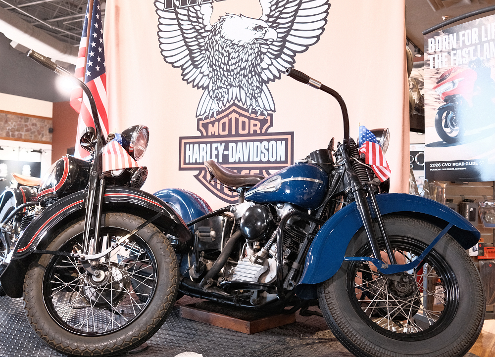 Vintage Harley-Davidson motorcycle displayed indoors with patriotic flags and large branded wall graphic behind