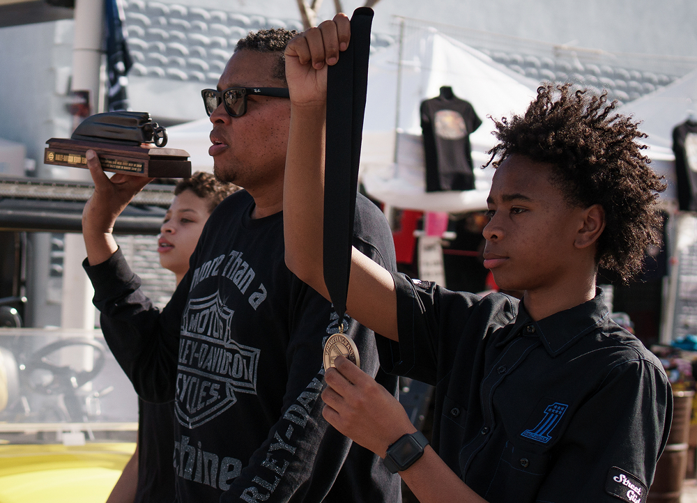 Influencer Traveling Tall and his two sons walks down Bethune Boulevard showing the trophies for winners of his bike show