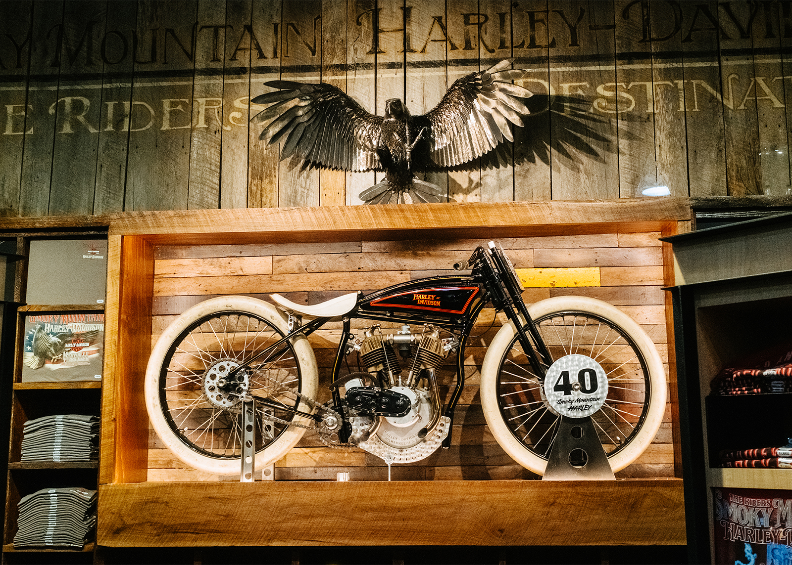 A very early Harley-Davidson on display in a wooden frame with a taxidermied bird with it’s wings spread sitting on top.