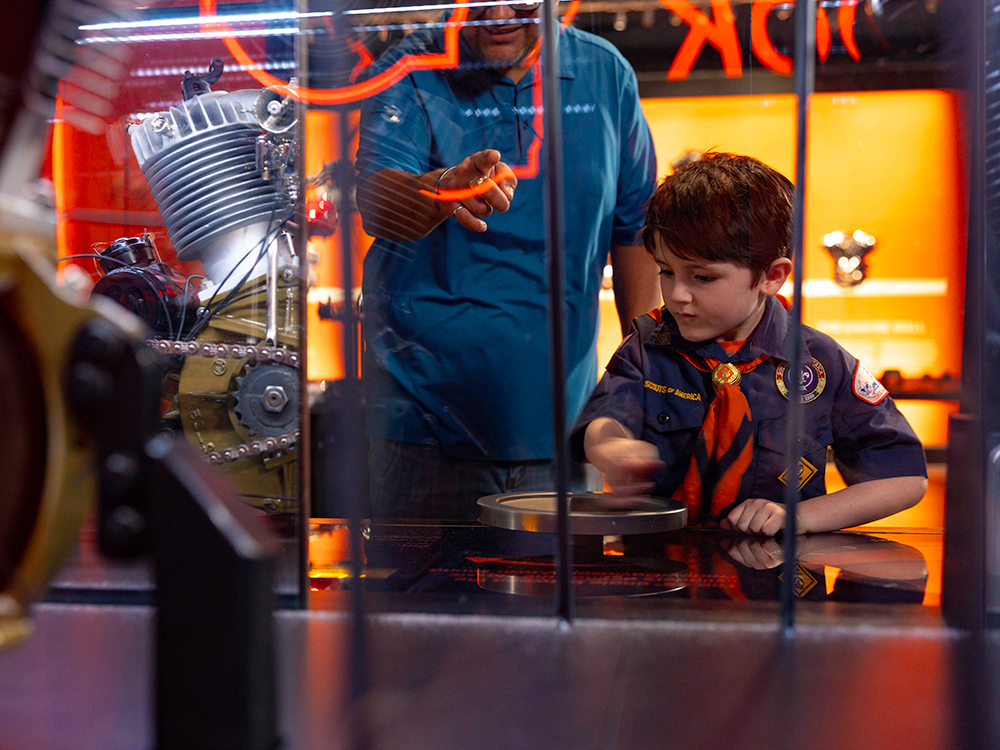 Child interacting with mechanical exhibit behind glass in museum