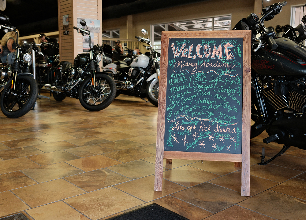 Welcome sign filled with Harley-Davidson Riding Academy graduate names stands among motorcycles on the showroom floor