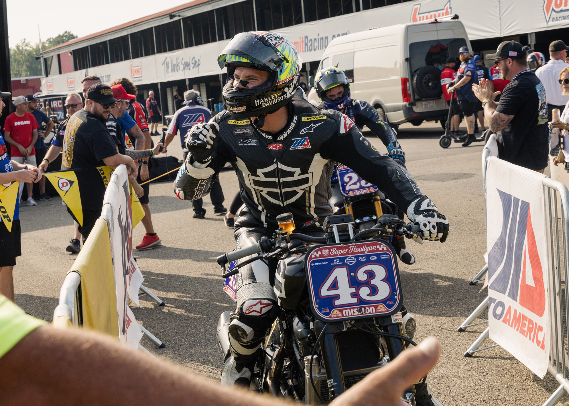James Rispoli rides into the paddock on bike #43, celebrating with a fist pump as fans cheer around him.