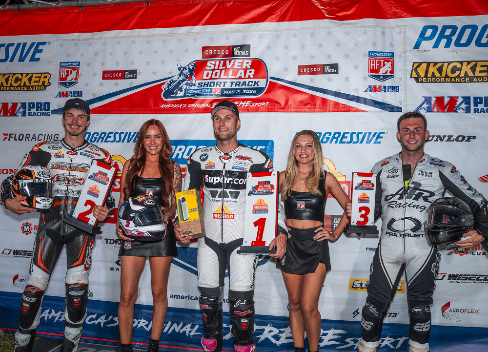 Top finishers pose on the podium with trophies and number boards after a flat track race event