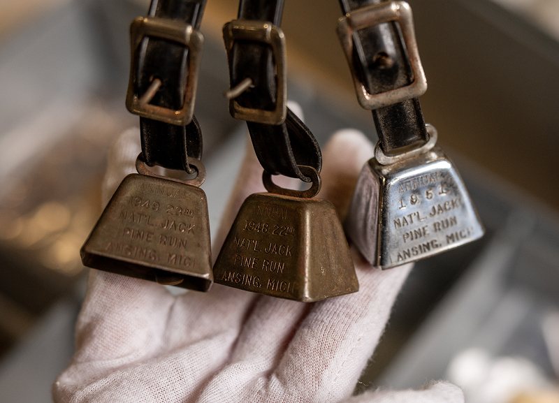 Close-up of three small vintage motorcycle awards shaped like bells, held in a gloved hand