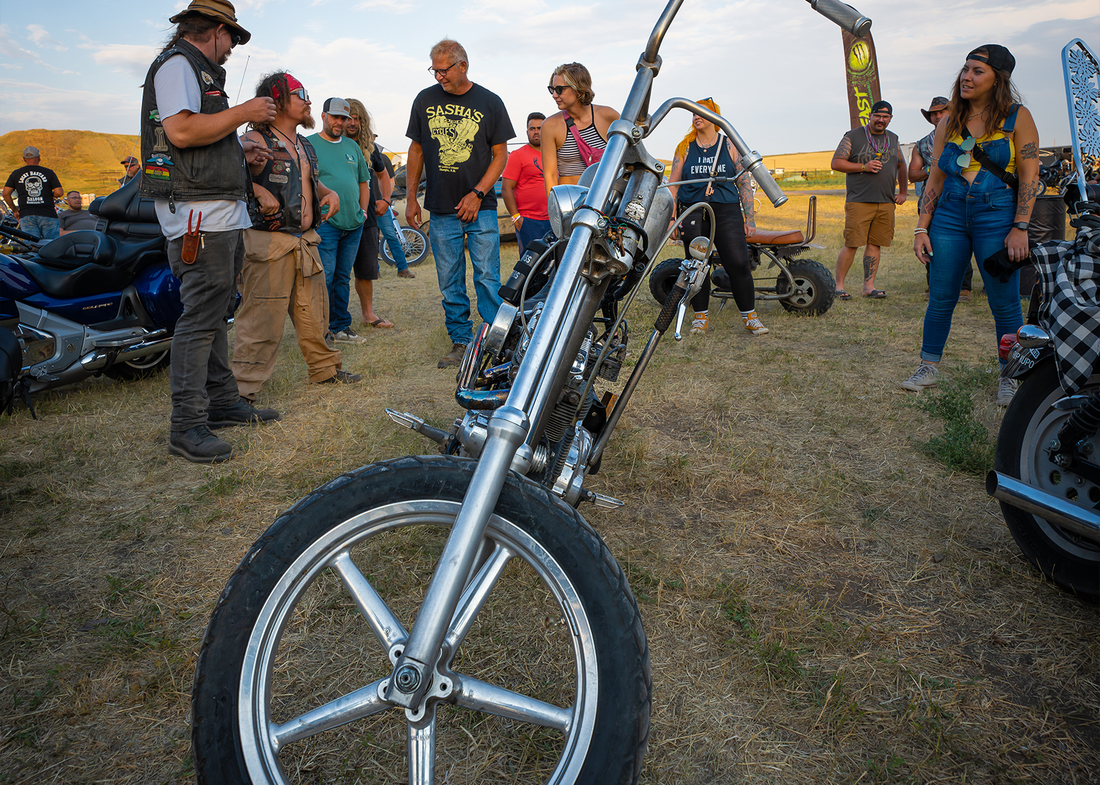 People stand around a bike with long front forks and a five-spoked wheel in an open field