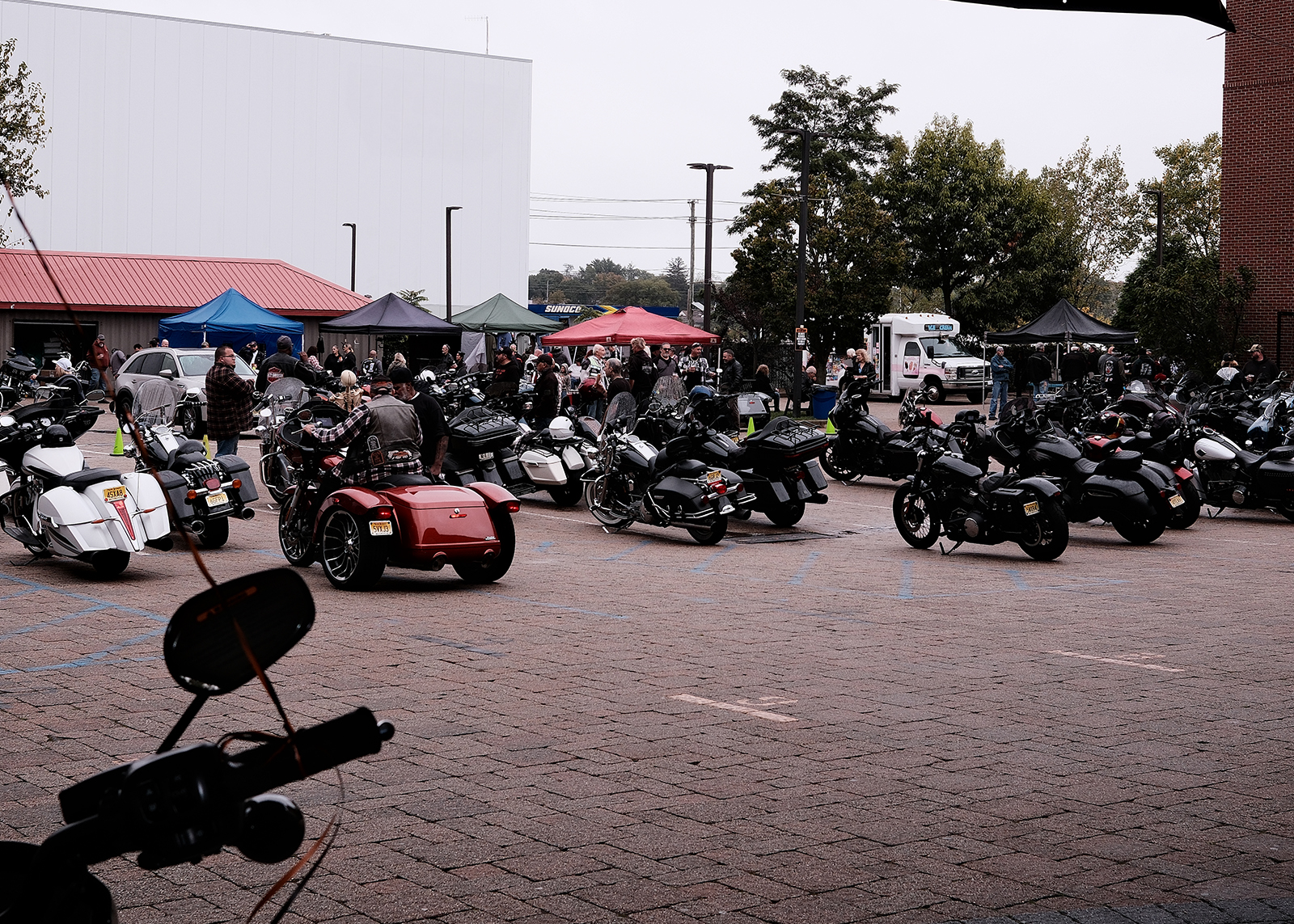 Bergen H-D’s 50 year anniversary party with tents and crowds in a parking lot filled with bikes and a red trike.