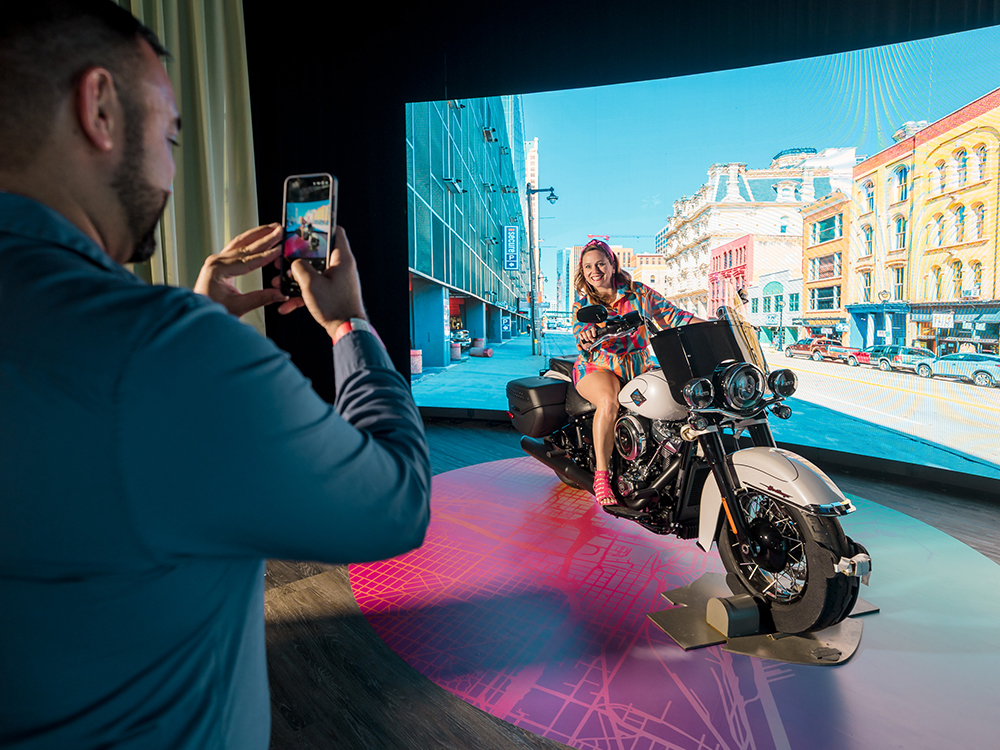 Visitor photographing rider on Harley-Davidson motorcycle exhibit