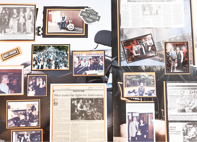 A wall of photos and newspaper articles documenting the history of Harley-Davidson of Madison