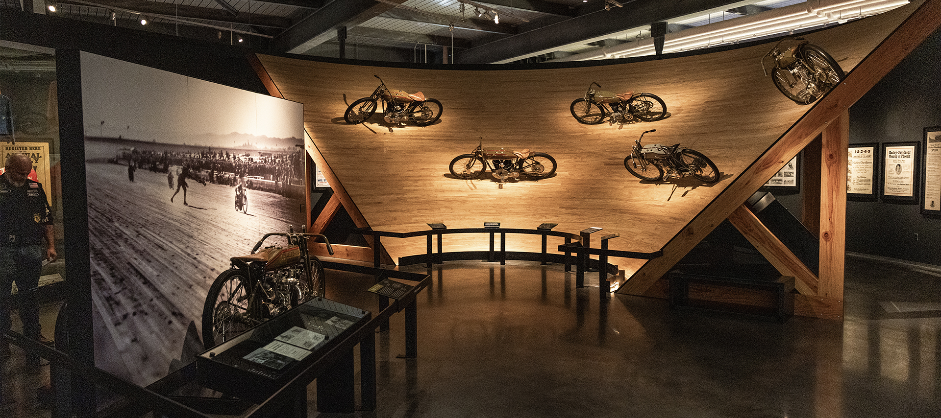 Exhibit at the Harley-Davidson Museum featuring vintage motorcycles mounted on a curved section of board track with historic photos