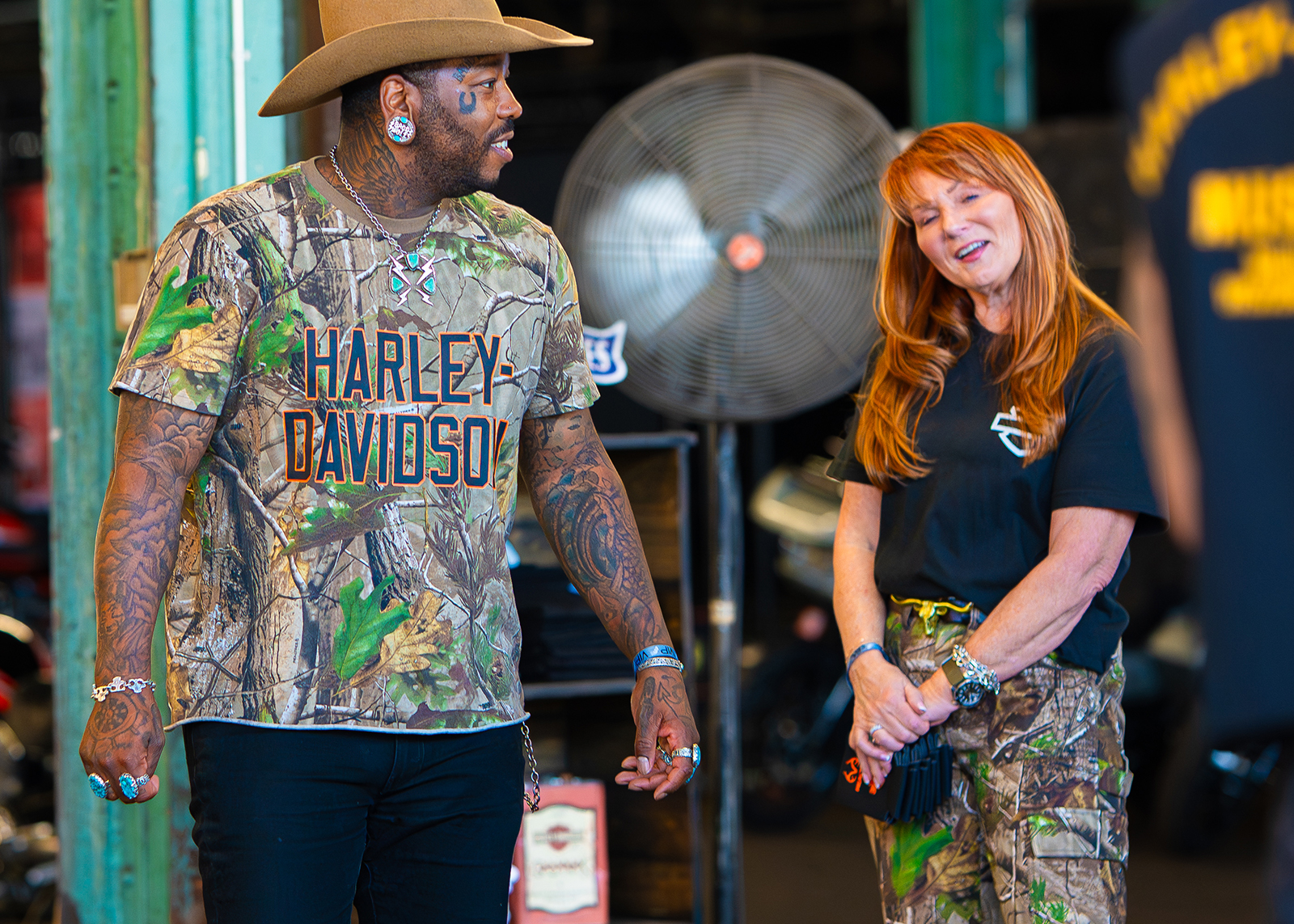 Two people in Harley-Davidson x Realtree camo gear chat at The Congregation Vintage Motorcycle Show.