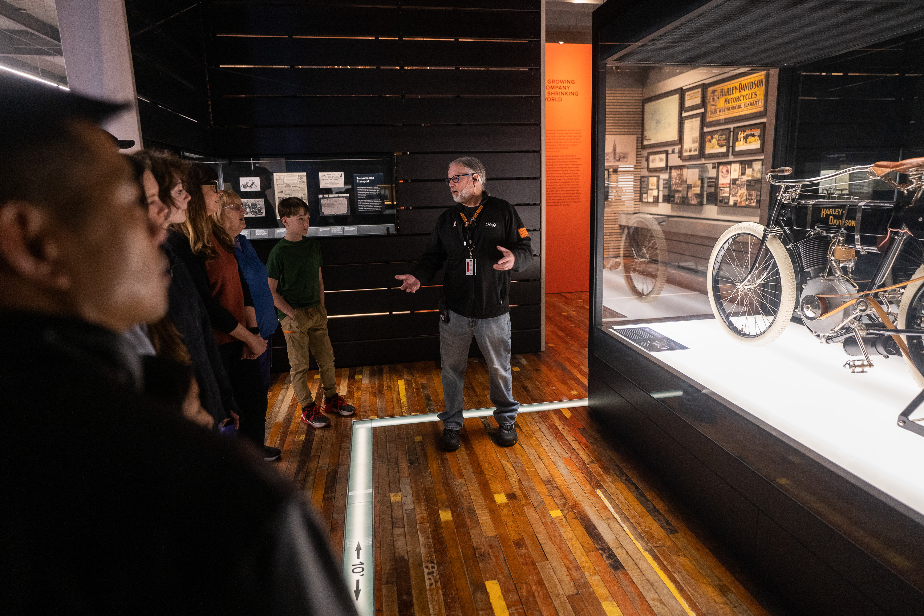 博物館ガイドが、ヴィンテージのハーレーダビッドソン・オートバイ展示のそばで来館者に話している