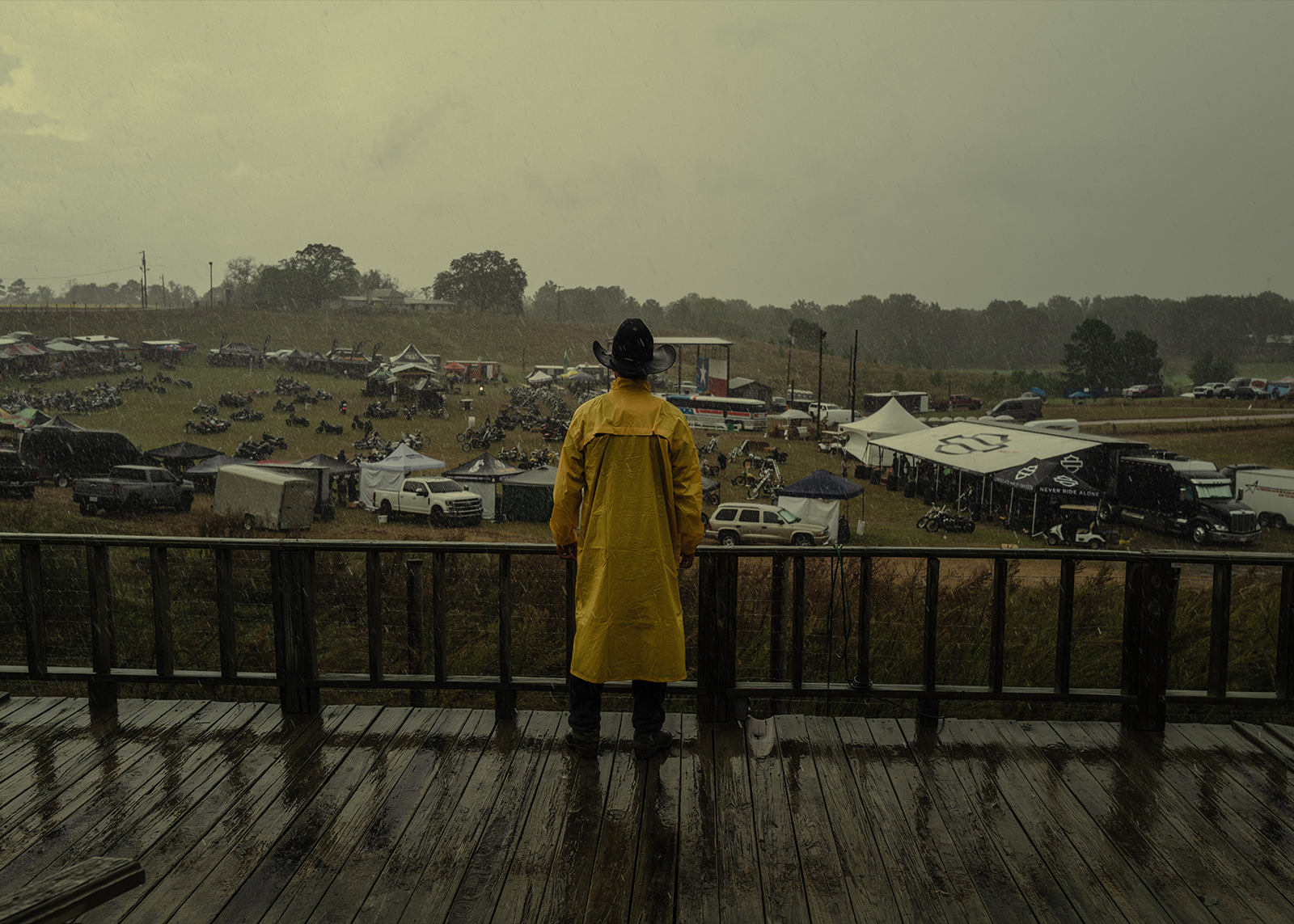 A person in a yellow raincoat and cowboy hat stands on a wet deck overlooking rainy weather at the Born Free Texas rally.