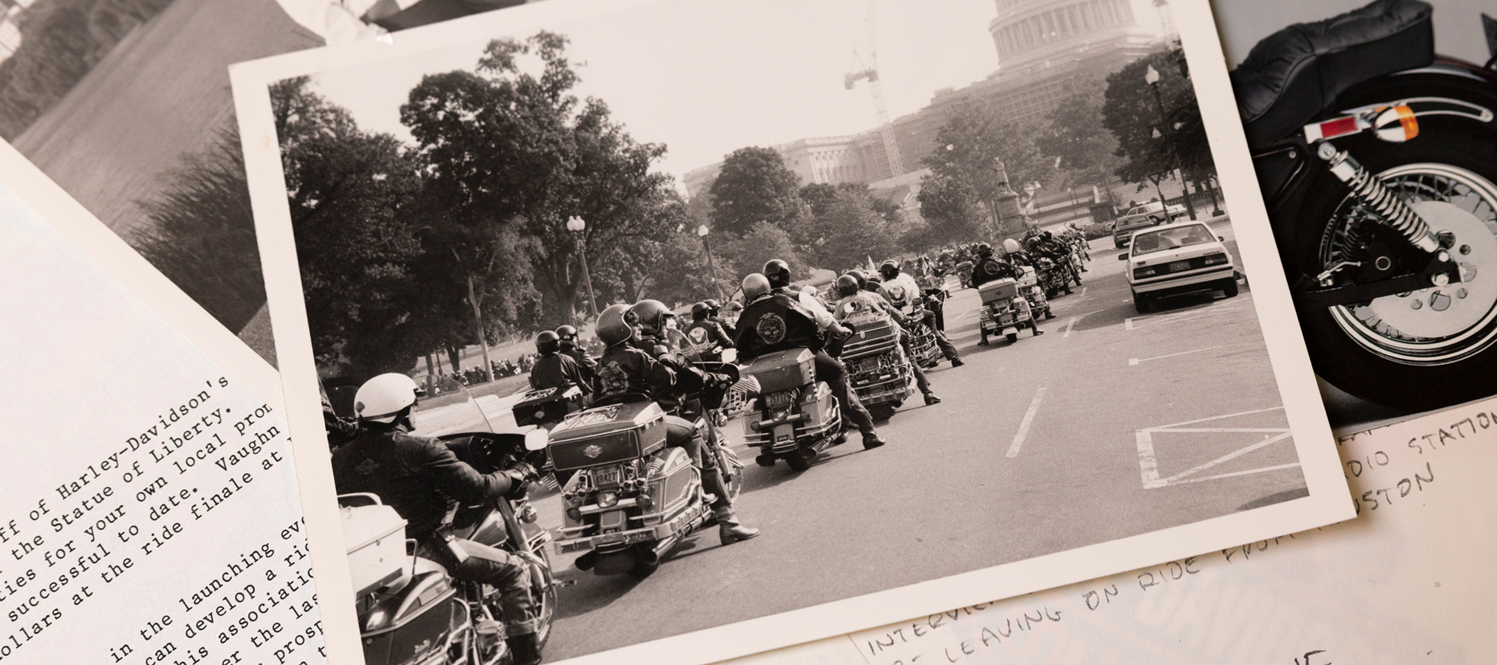 Black-and-white photo of a motorcyclist procession riding toward the U.S. Capitol, laying among papers