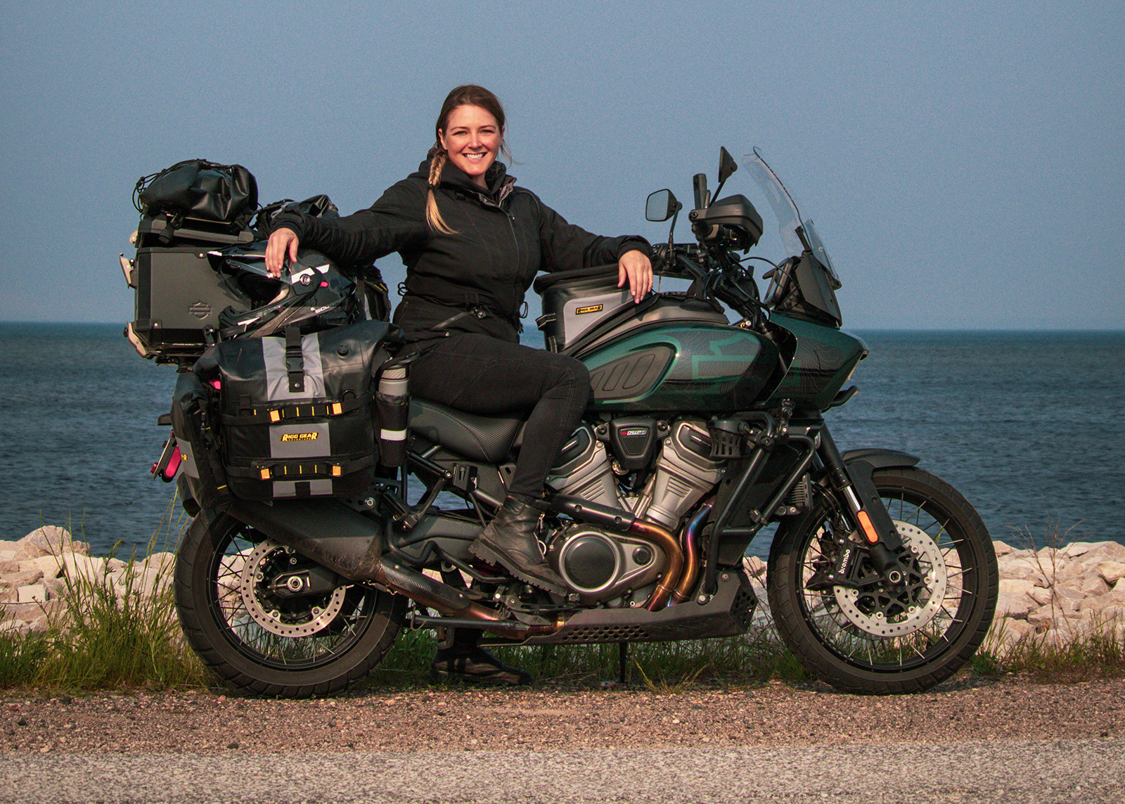 The author sits on her fully loaded Harley-Davidson Pan America motorcycle parked by the water.