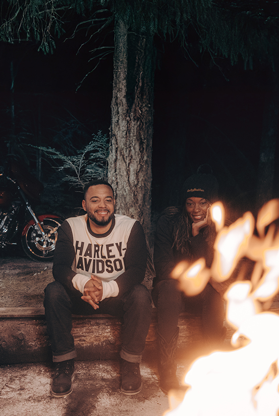 Man in Harley-Davidson shirt and woman sitting by a fire