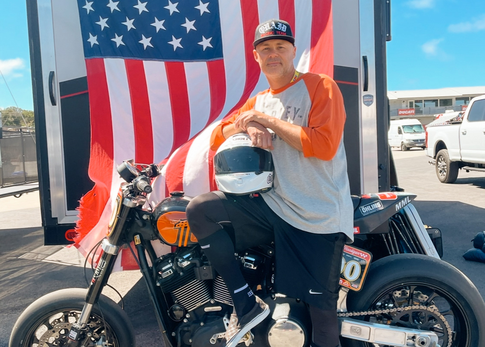 A member of Quaid’s racing team poses with a race bike in front of an American flag.