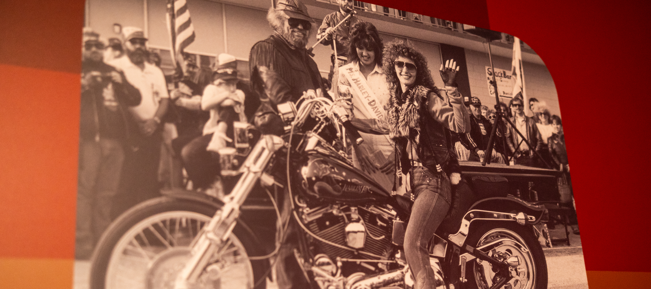 Vintage photo of Gail Anderson in her one-off vest lined with fox pelt, sitting on a motorcycle in a parade with Willie G. Davidson